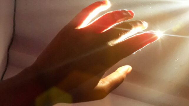 A hand in front of an open window, letting in sunlight that causes it to appear glowing