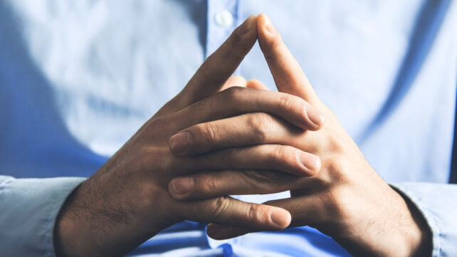 High contrast image of a man in a blue shirt, with hands clasped in front of his chest