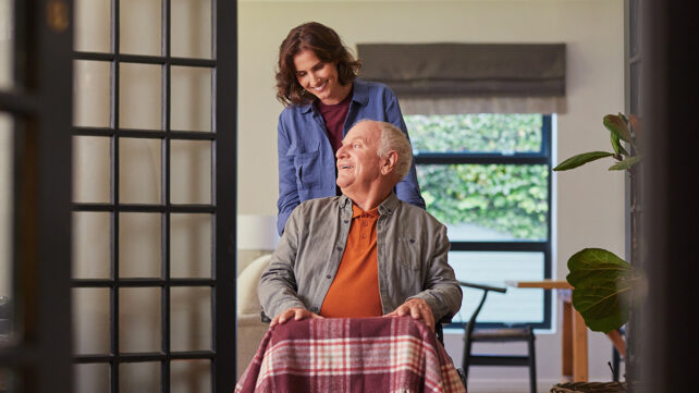 Senior man sitting on a wheelchair while his daughter assists him