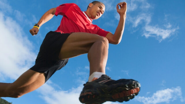 Low angle view of a man in a red t-shirt running, against a bright blue sky