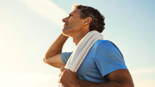 A middle-aged man with an exercise towel over his shoulders is gazing towards the sky with a hopeful look