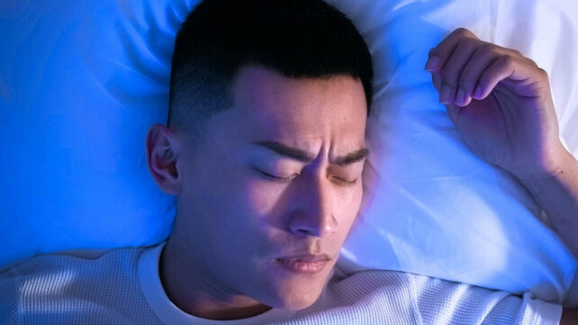 A dark-haired man sleeping in high-contrast blue surroundings
