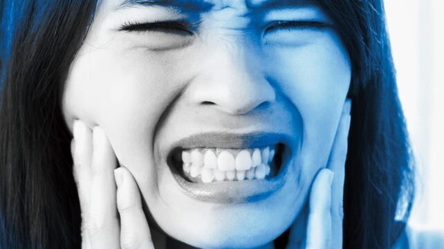 A woman holding her jaw and grimacing