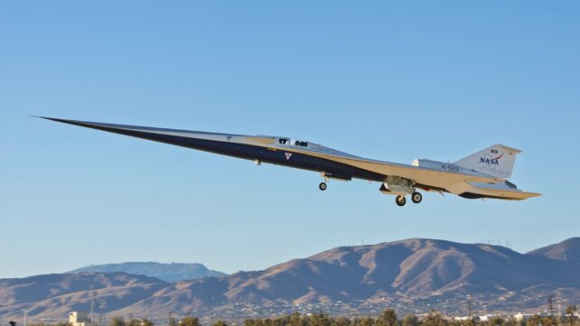 NASA/Lockheed Martin X-59 experimental quiet-supersonic jet lifting off over desert foothills, landing gear down, very long needle nose.